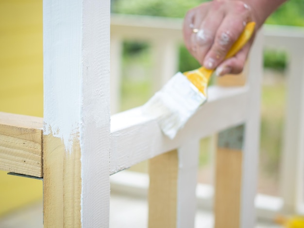 La mano de un hombre con un pincel pinta una viga de madera con pintura blanca.