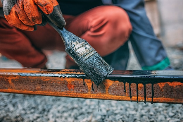 La mano del hombre pinta un poste de metal con un pincel con pintura negra