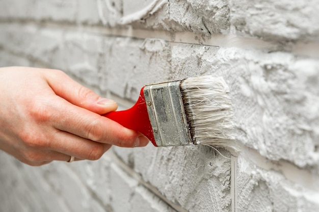 Mano de hombre pintada con pincel de pared de ladrillo blanco. Trabajo de renovación. Fondo blanco.