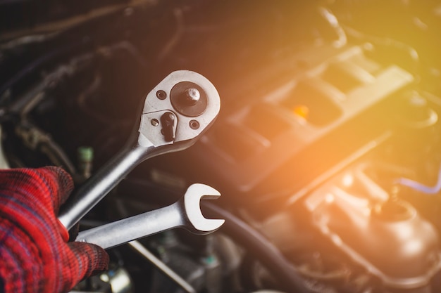 La mano del hombre profesional mecánico sostiene una llave herramientas con fondo borroso del motor del coche en el garaje de reparación de vehículos, concepto de mantenimiento automotriz.