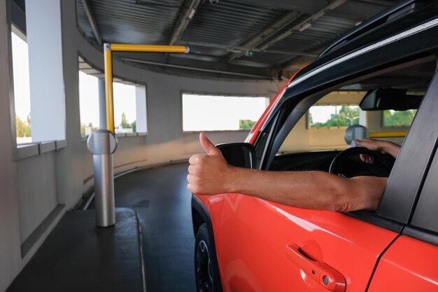 Una mano de un hombre con un pulgar arriba cerca del coche al entrar en un estacionamiento subterráneo de seguridad de estacionamiento