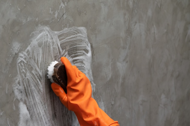 La mano del hombre que lleva guantes de goma naranja se usa para convertir la limpieza de maleza en el concreto