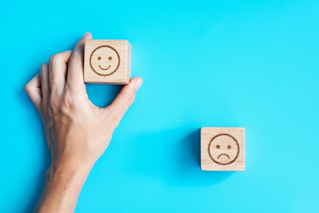 Mano de hombre que sostiene el bloque de cara de emoción El cliente elige Emoticon para las revisiones de los usuarios Clasificación de calificación del servicio evaluación de satisfacción de revisión del cliente y concepto de retroalimentación