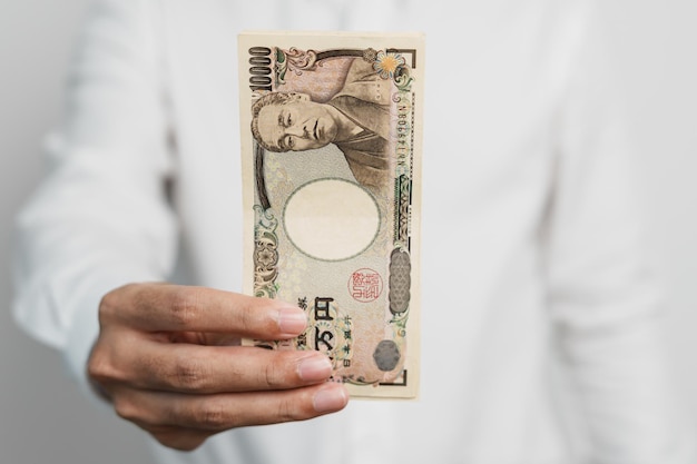 Mano de hombre que sostiene la pila de billetes de yen japonés Dinero de mil yenes Japón efectivo Recesión fiscal Economía Inflación Finanzas de inversión y conceptos de pago de compras