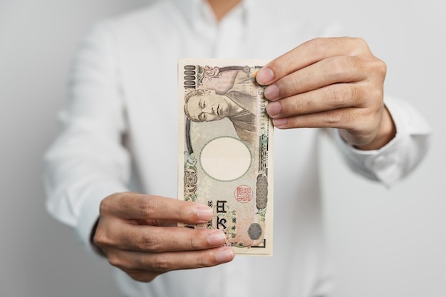 Mano de hombre que sostiene la pila de billetes de yen japonés Dinero de mil yenes Japón efectivo Recesión fiscal Economía Inflación Finanzas de inversión y conceptos de pago de compras