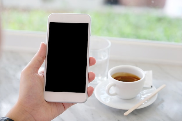 Mano del hombre que sostiene el teléfono inteligente blanco con pantalla en blanco sobre fondo