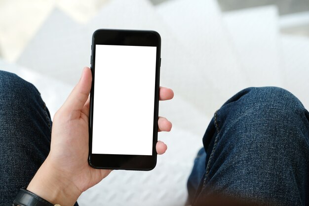 Mano del hombre que sostiene el teléfono inteligente negro con pantalla en blanco sobre fondo para maqueta