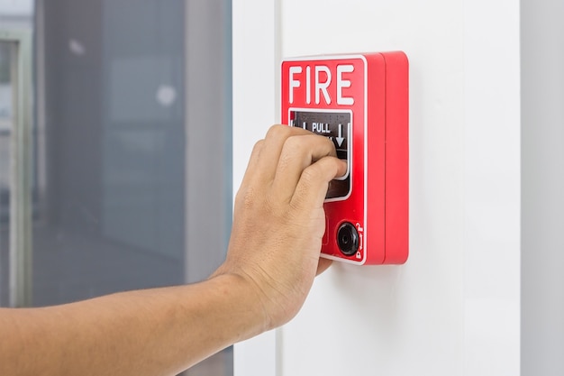 Mano del hombre que tira del interruptor de la alarma de incendio en la pared blanca como fondo para el caso de emergencia