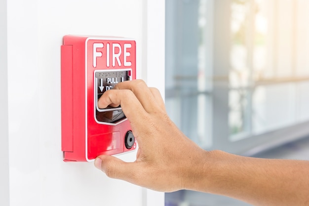 Mano del hombre que tira del interruptor de la alarma de incendio en la pared blanca como fondo para el caso de emergencia
