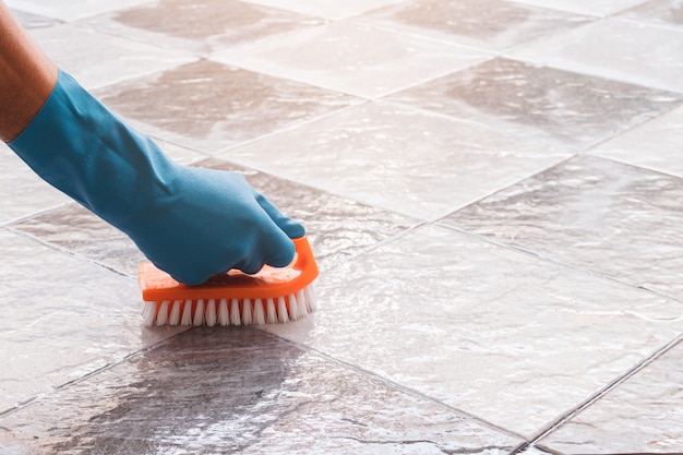 Foto la mano del hombre que usa guantes de goma azules se utiliza para convertir la limpieza de matorrales en el piso de baldosas.