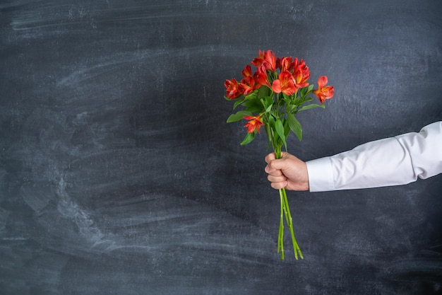 La mano de un hombre con un ramo de flores sobre un fondo de pizarra copyspace