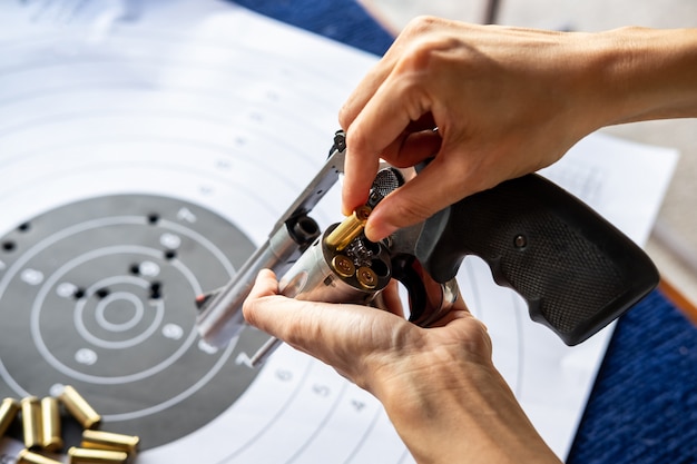 Mano del hombre recargando revólver de pistola con balas y objetivo