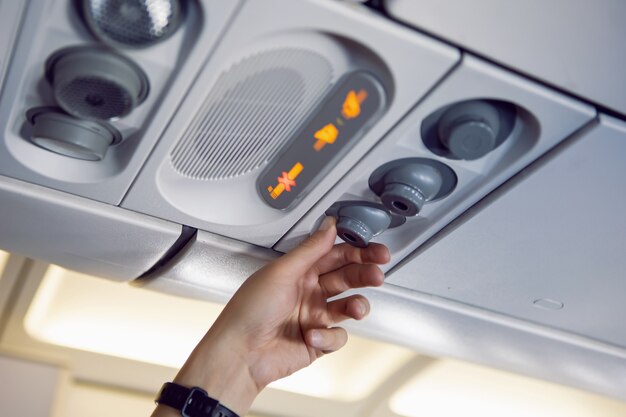 La mano del hombre regula el aire y la luz en el avión en el panel de instrumentos de arriba