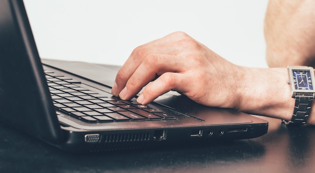 Mano de un hombre con un reloj de pulsera escribiendo texto en el teclado en el trabajo en la oficina