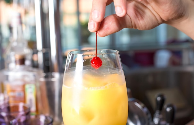 Mano de hombre sacando cereza marrasquino del vaso con bebida alcohólica con hielo y jugo de naranja.