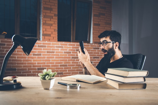 Mano de hombre sorprendido con teléfono con libros en el escritorio