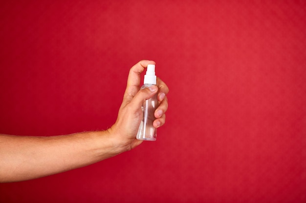 Mano de hombre sosteniendo un aerosol desinfectante sobre fondo rojo de estudio, equipo de protección contra coronavirus, aerosol desinfectante antiséptico, desinfección, protección antiséptica para las manos durante la pandemia de COVID-19