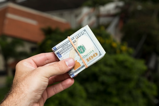 Mano de hombre sosteniendo billetes de un dólar frente a un paisaje de la ciudad