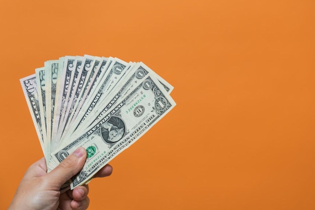 Mano de hombre sosteniendo billetes de dólar sobre fondo naranja