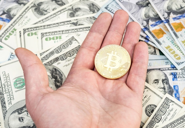 Mano de hombre sosteniendo bitcoin dorado sobre fondo de dólares estadounidenses
