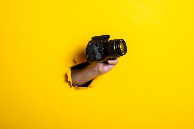 Mano de hombre sosteniendo una cámara sobre un fondo amarillo brillante