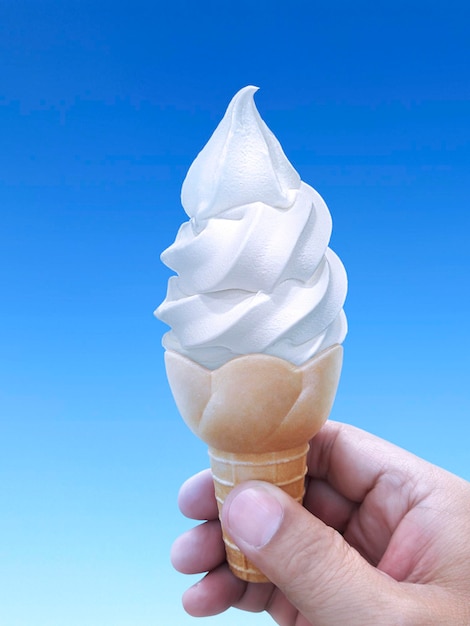 Mano de hombre sosteniendo un cono de helado en el fondo del cielo azul