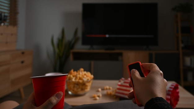 Mano de hombre sosteniendo el control remoto viendo la televisión en casa Concepto de entretenimiento y actividades de ocio