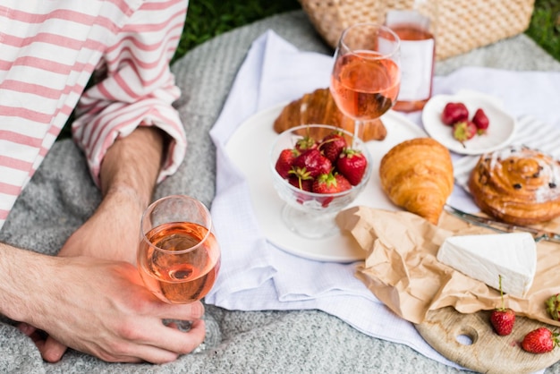 Mano de hombre sosteniendo una copa de vino rosado picnic de verano con queso y vino