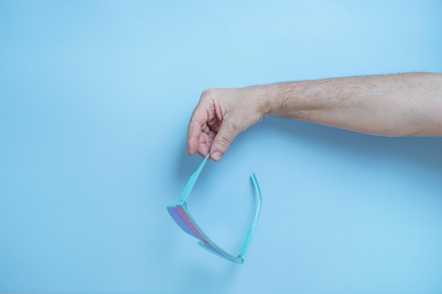 La mano de un hombre sosteniendo gafas de sol azules.