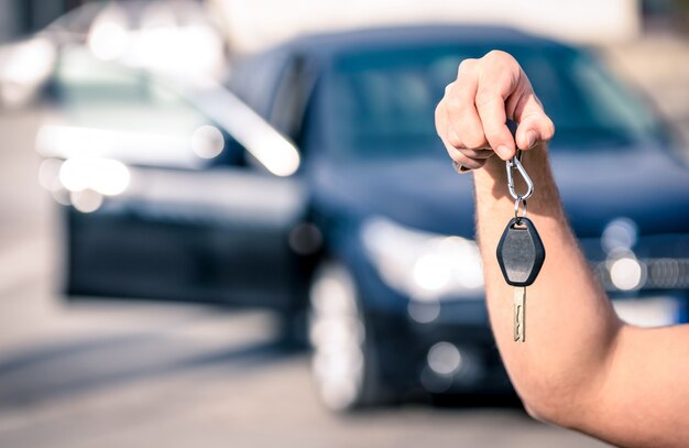 La mano del hombre sosteniendo las llaves del coche moderno listas para alquilar