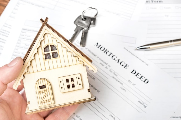 Mano de hombre sosteniendo modelo de casa sobre escritura de hipoteca Concepto inmobiliario