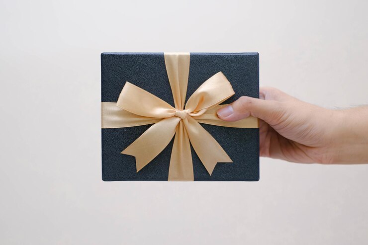 La mano del hombre sosteniendo una pequeña caja de regalo azul envuelta con cinta de oro en un fondo blanco aislado