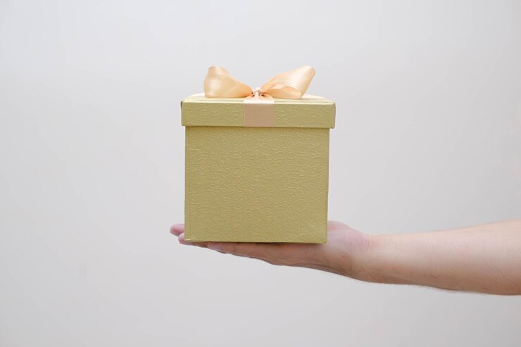 La mano del hombre sosteniendo una pequeña caja de regalo de oro envuelta con cinta de oro en un fondo blanco aislado