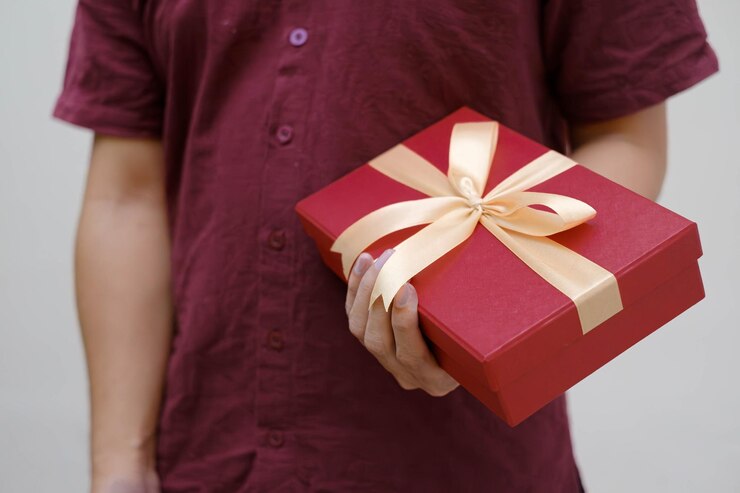 La mano del hombre sosteniendo una pequeña caja de regalo roja envuelta en cinta de oro