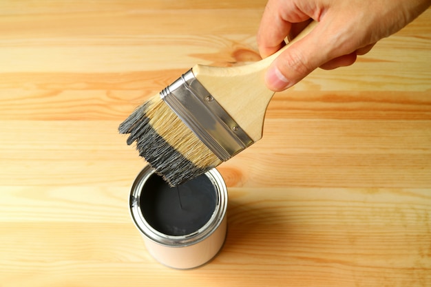 La mano del hombre sosteniendo el pincel con la pintura cayendo después de sumergirlo en la lata de pintura