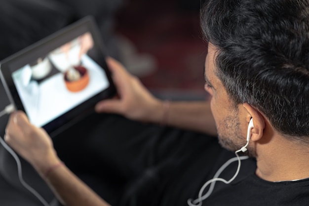 Mano de hombre sosteniendo con tableta digital viendo la clase magistral de cocina en línea