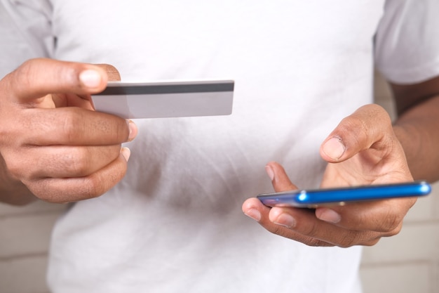 Foto mano de hombre sosteniendo tarjeta de crédito y usando teléfonos inteligentes para compras en línea