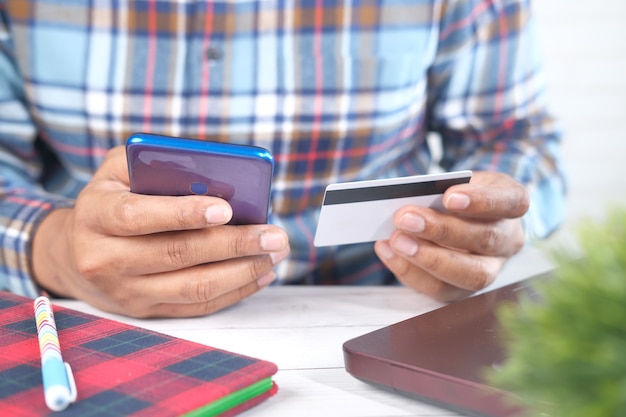 Mano de hombre sosteniendo tarjeta de crédito y usando teléfonos inteligentes para compras en línea