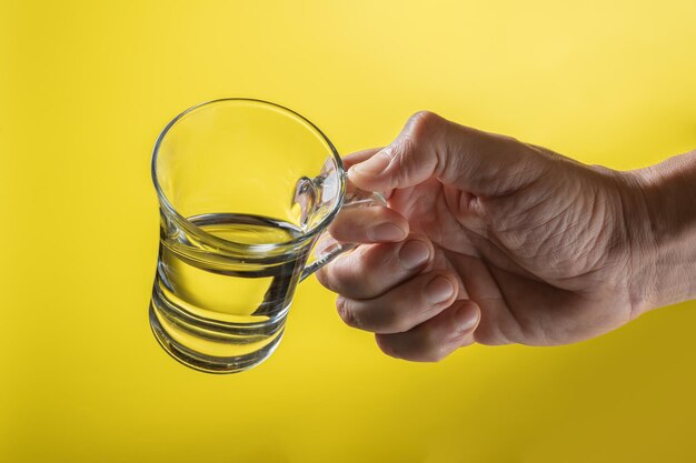 Una mano de hombre sosteniendo una taza de agua limpia en un fondo amarillo brillante