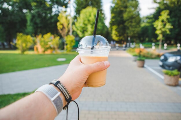 Mano de hombre sosteniendo una taza con bebida refrescante caminando por el parque público de verano