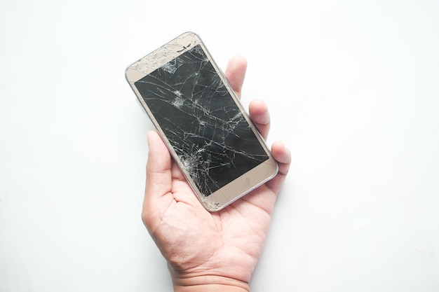 Mano de hombre sosteniendo un teléfono inteligente roto sobre fondo blanco.