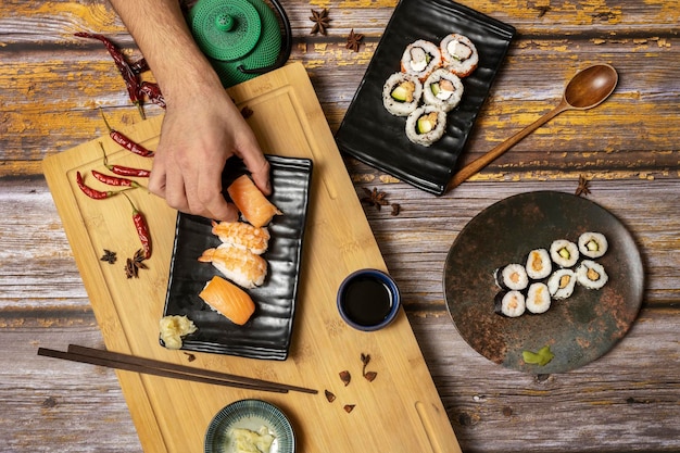Mano de hombre sosteniendo un trozo de sushi nigiri de salmón noruego de un conjunto de platos de comida japonesa con palillos y salsa de soja
