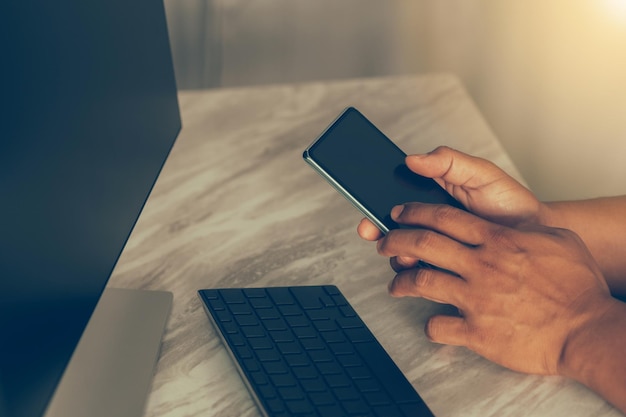 Mano de hombre sosteniendo usando un teléfono inteligente con una computadora portátil para el enfoque selectivo de negocios