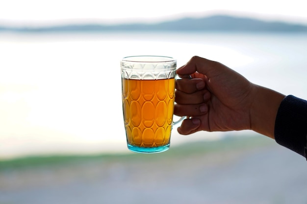 la mano de un hombre sosteniendo un vaso de té junto al lago