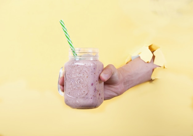 La mano de un hombre sostiene un batido fresco de leche y cerezas en un frasco de vidrio