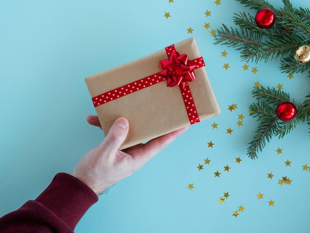 La mano de un hombre sostiene una caja de regalo con un lazo rojo sobre un fondo navideño.