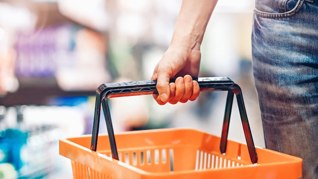 La mano del hombre sostiene una cesta vacía en el supermercado. Concepto de compras