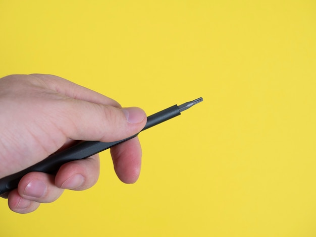 La mano de un hombre sostiene un destornillador pequeño con una boquilla torx sobre un fondo amarillo brillante. Copia espacio