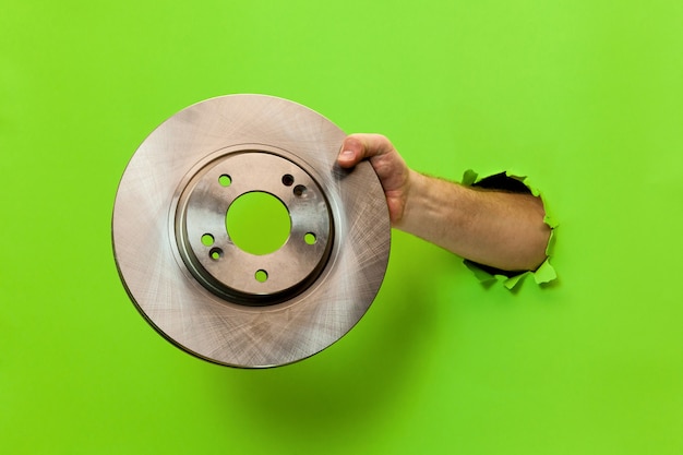 La mano de un hombre sostiene un disco de freno de automóvil a través de papel verde rasgado. Mano a través de papel verde rasgado