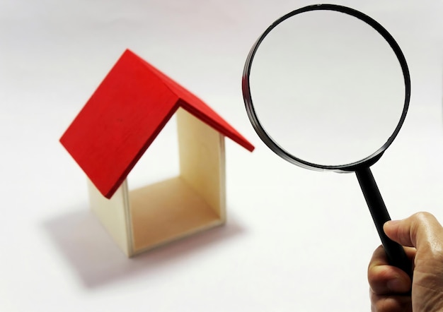 Una mano de hombre sostiene una lupa sobre una casa en miniatura Búsqueda de bienes raíces Inspección de casa